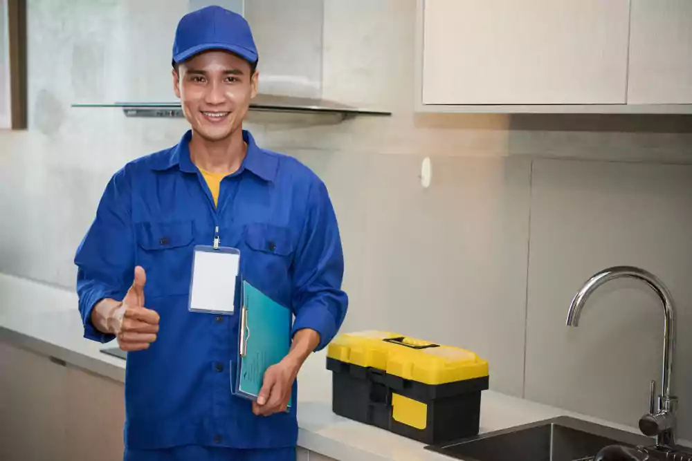cheerful asian plumber standing near kitchen sink showing thumb up